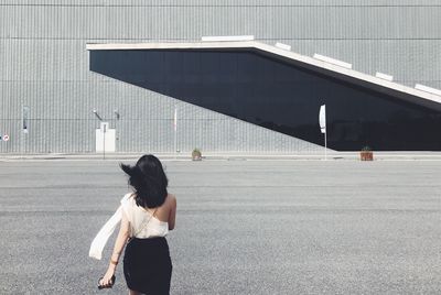 Rear view of woman walking on road against building