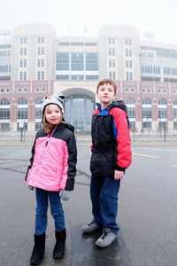 Full length of siblings standing on road in city during foggy weather