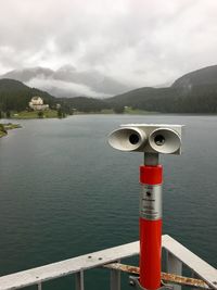 Close-up of coin-operated binoculars by lake against sky