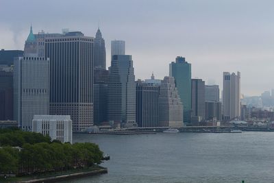 Modern buildings by river against sky in city