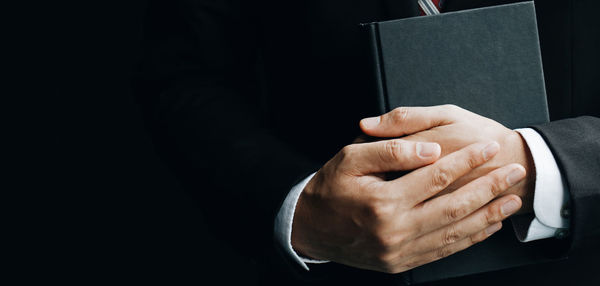 Midsection of man holding cigarette at black background