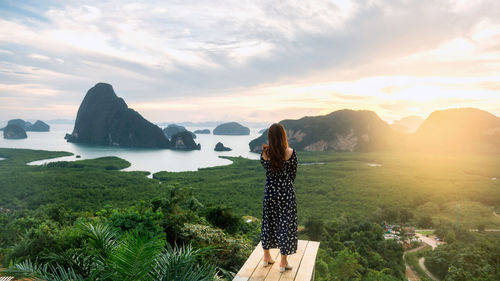 Rear view of woman standing on mountain against sky during sunset