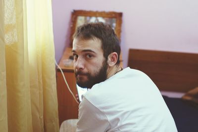 Portrait of man holding mobile phone while sitting on bed at home