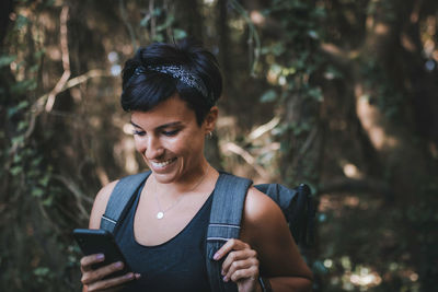 Smiling woman using smart phone while standing in forest