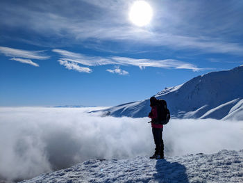 Side view of backpacker standing on snowcapped mountain against sky