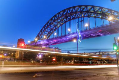 Light trails on bridge in city against sky at night