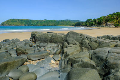 Rocks on beach against clear blue sky