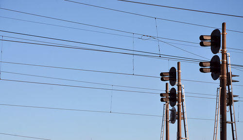 Low angle view of power lines and railway signals against clear blue sky