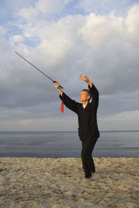 Young man practicing tai chi at beach against cloudy sky