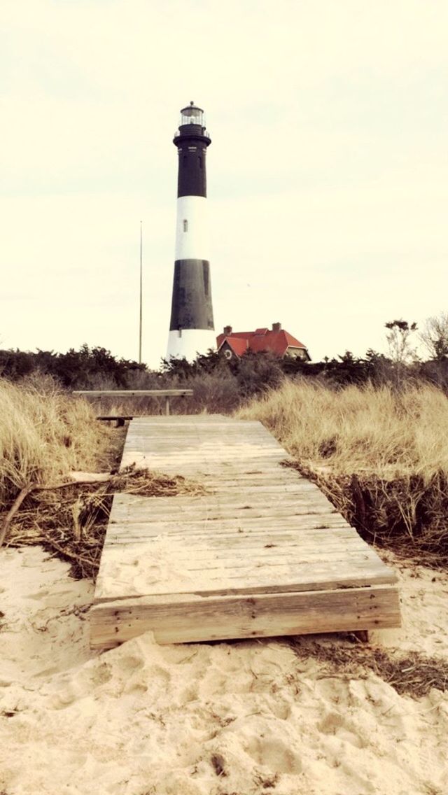 lighthouse, built structure, architecture, building exterior, guidance, sky, protection, direction, safety, sea, water, security, tranquility, tranquil scene, day, nature, beach, grass, outdoors, sand