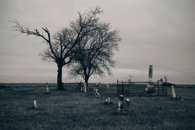 Tombstones and bare trees on field against sky