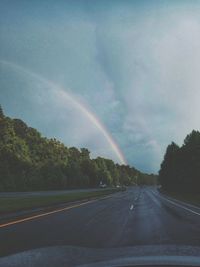 Rainbow over road against sky