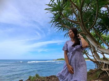 Young woman standing at beach against sky