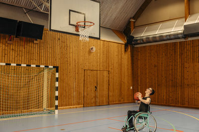 Girl playing basketball while sitting on wheelchair at sports court