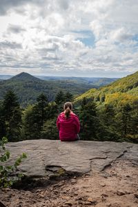 Rear view of woman sitting on mountain against sky