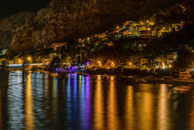 Illuminated city by river at night