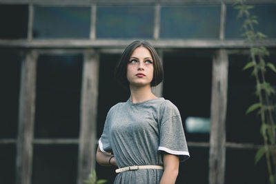 Beautiful young woman looking away while standing against windows