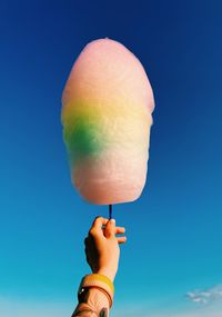 Cropped hand holding ice cream against blue background