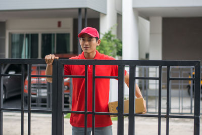 Delivery man standing at closed gate against buildings