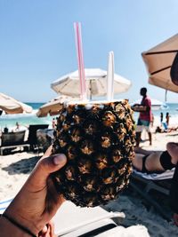 Close-up of hand holding drink in pineapple against sky