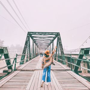 Rear view of woman standing on footbridge against sky