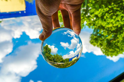 Cropped hand holding crystal ball against blue sky