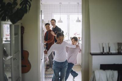 Gay couple looking at daughters running while playing at home