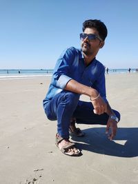 Young man wearing sunglasses on beach against sky