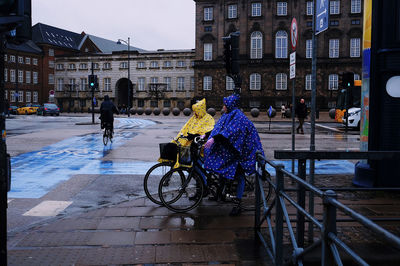 People riding bicycle on street against buildings in city