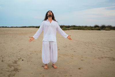 Stock photo of adult man with long hair asking for god in the beach.