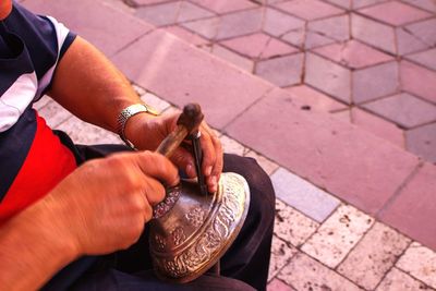 Midsection of man carving metal while sitting on footpath