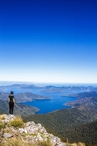 Rear view of man standing on mountain against blue sky