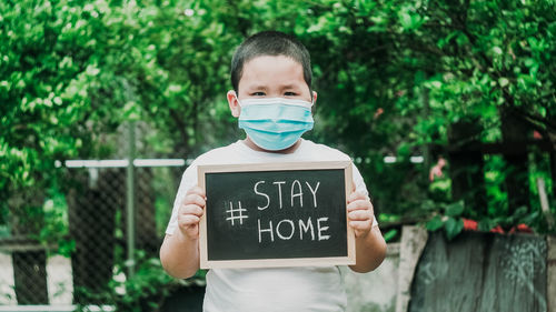 Portrait of boy wearing flu mask holding slate standing outdoors