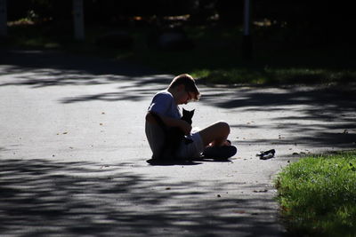Side view of boy with cat sitting on road 
