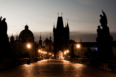 Illuminated charles bridge leading towards silhouette historic building at dusk