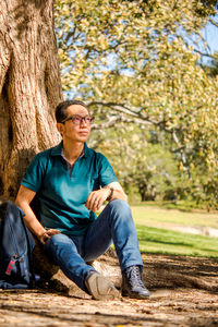 Thoughtful man sitting against tree trunk at park