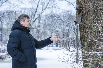 Man feeds curious squirrel from his hand in winter snowy park. winter color of animal.