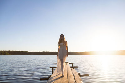 Beautiful girl in a white dress, walking along a wooden pier on the bank of a river or a lake