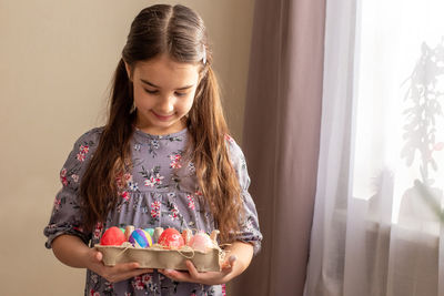 A cute little girl holds a cardboard tray with colorful eggs