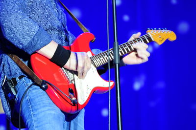 Midsection of man playing guitar on stage at concert