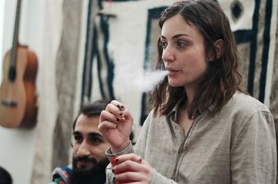 Close-up of young woman looking away smoking by friend