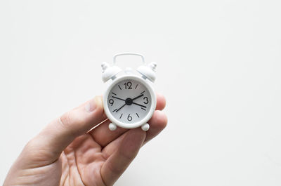 Close-up of hand holding clock against white background