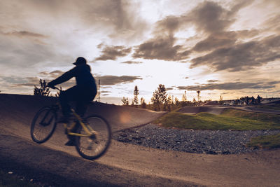 Man riding bicycle against sky during sunset