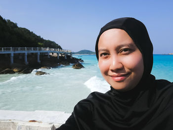 Portrait of smiling woman wearing hijab against seascape