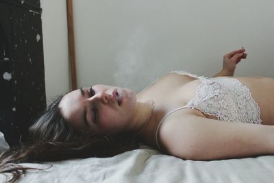 Beautiful woman lying in lingerie on bed while smoking cigarette at home