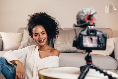 Smiling woman sitting at home while getting filmed on camera