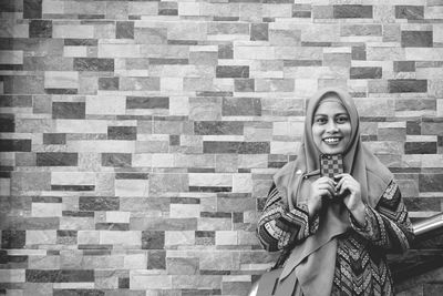 Portrait of smiling young woman standing against brick wall