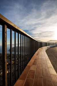 Empty footpath by railing against sky