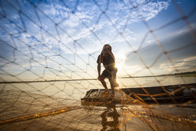 Fisherman holding fishing net at sea against sky