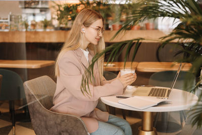 Portrait of a business woman student smiling drinking coffee working online using a laptop in a cafe